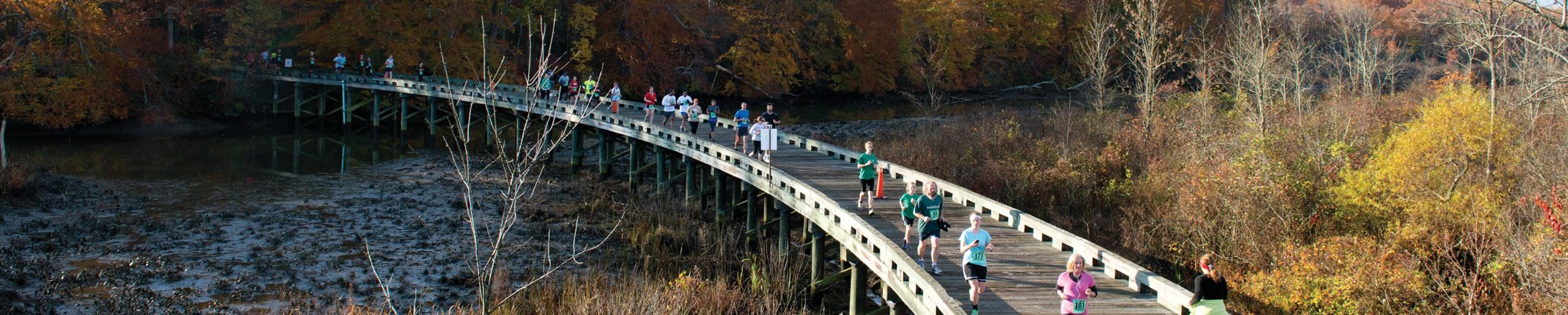 race of men and women running on a pedestrian bridge over a river